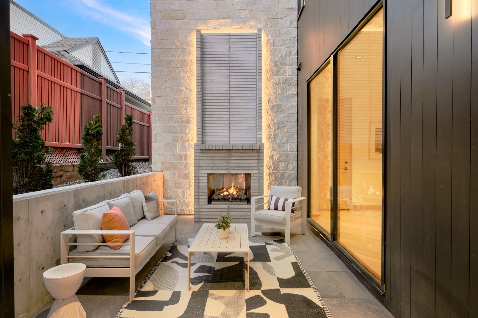 Modern patio with stone fireplace and warm interior glow — Synergistic Development Denver